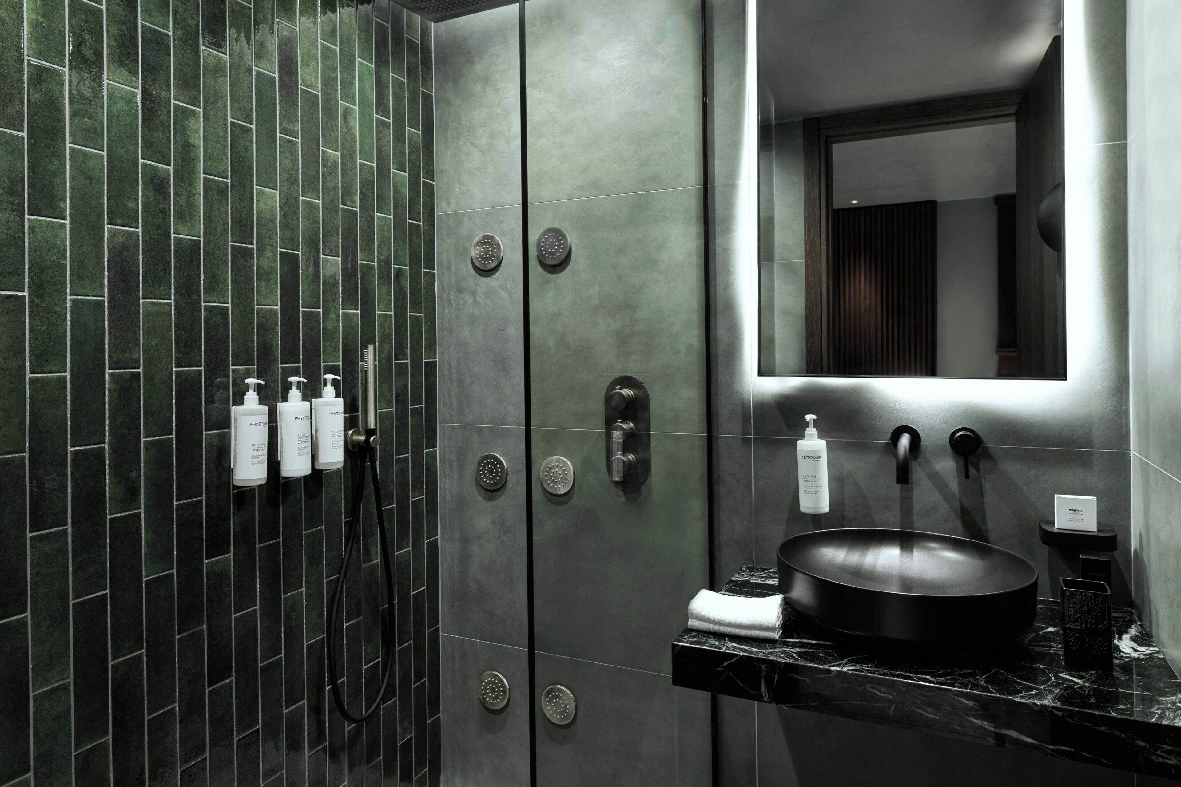 Un baño moderno con un espejo grande, un lavabo negro y una ducha con varios controles.