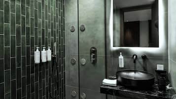 Un baño moderno con un espejo grande, un lavabo negro y una ducha con varios controles.
