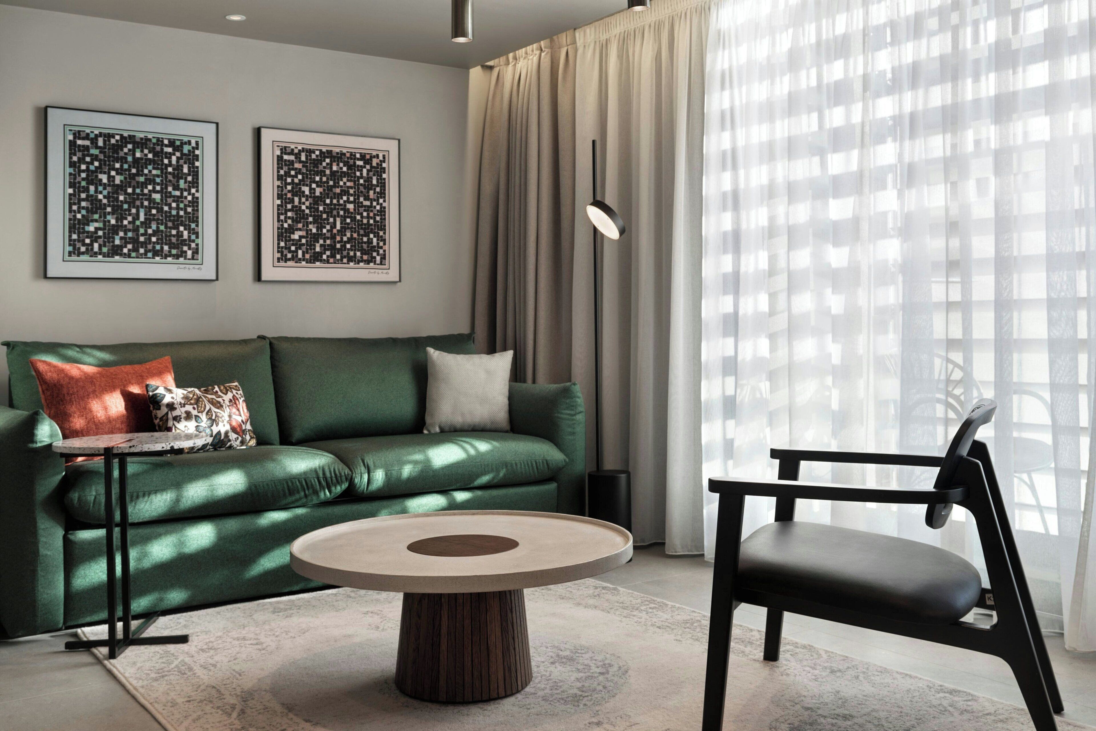 A modern living room with a green sofa, a round coffee table, a black chair, and two framed abstract artworks on the wall.
