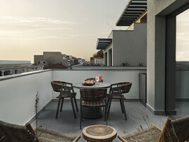 Terraza en la azotea con una mesa redonda y cuatro sillas de mimbre, con vistas a un paisaje urbano.