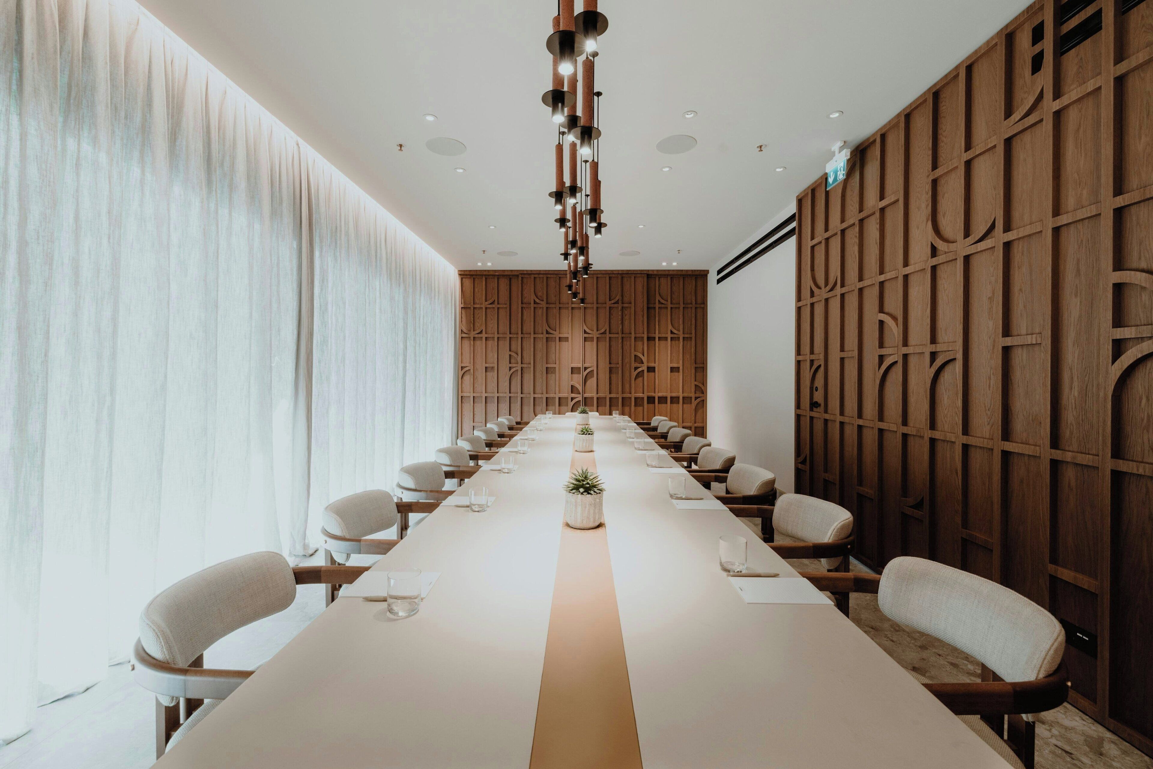 Una sala conferenze con un lungo tavolo, sedie e un pannello di legno a parete.