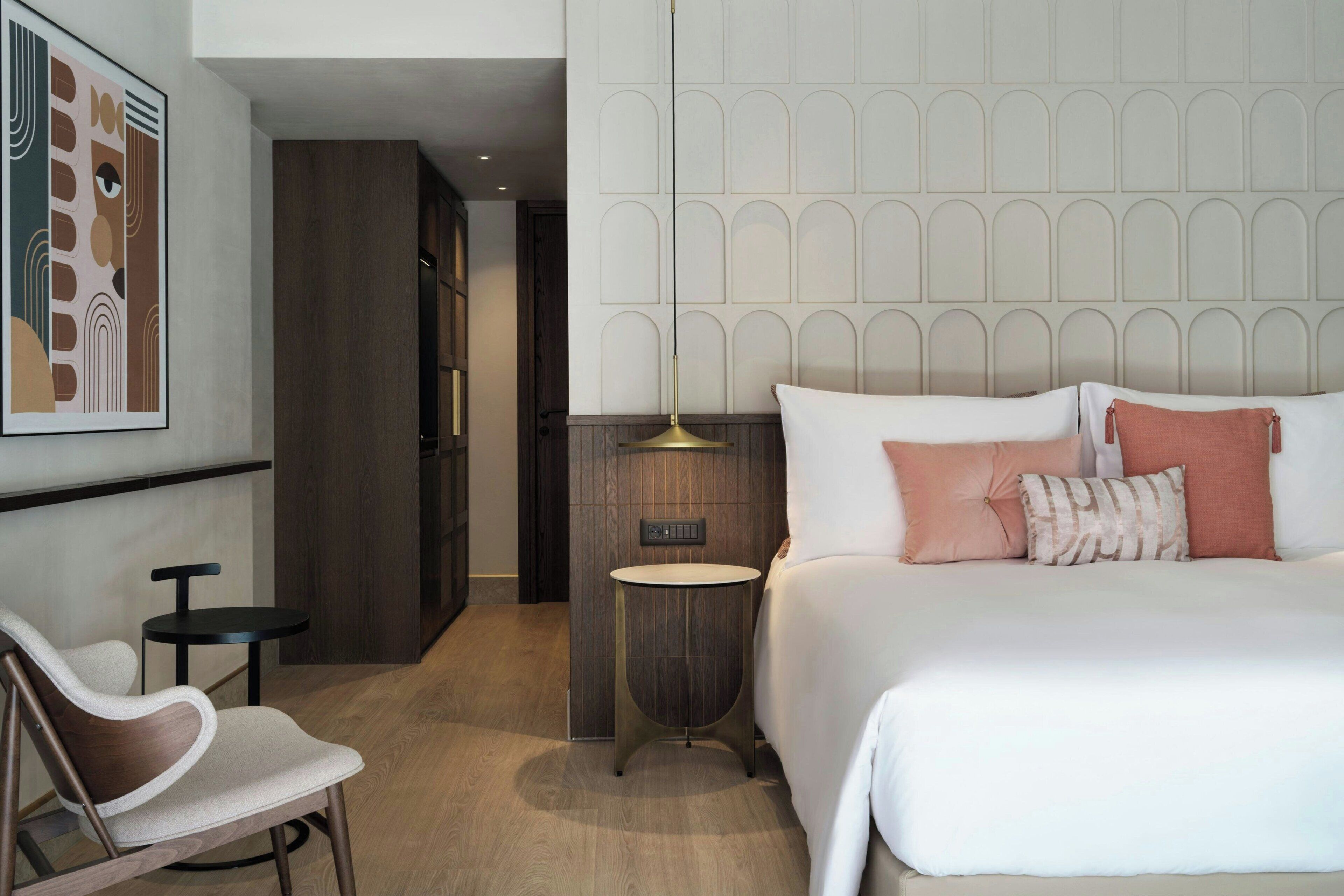 A modern hotel room with a large bed, a small round table, a chair, and a decorative wall panel.