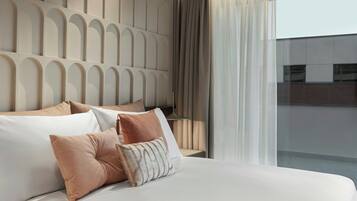 A modern hotel room with a large bed, a headboard with a geometric pattern, and a view of the city through large windows.