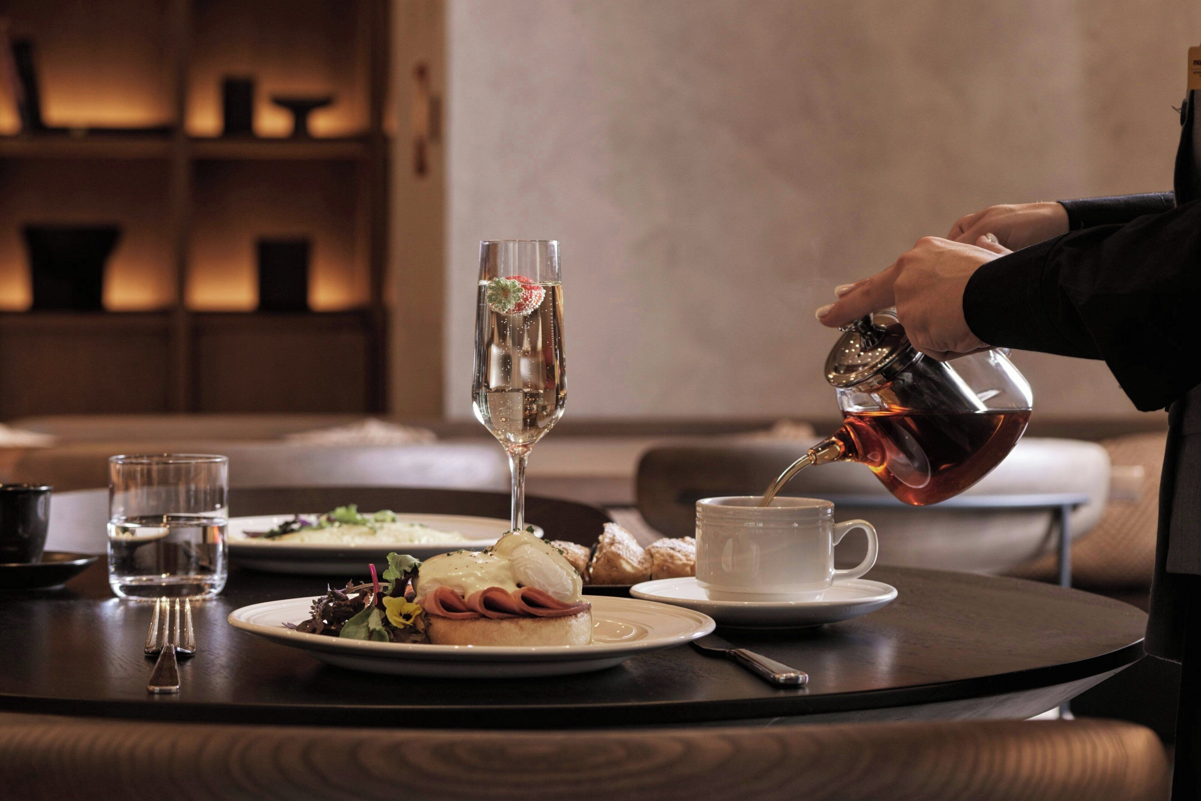 A dining table with a plate of food, a glass of water, and a cup of tea being poured.