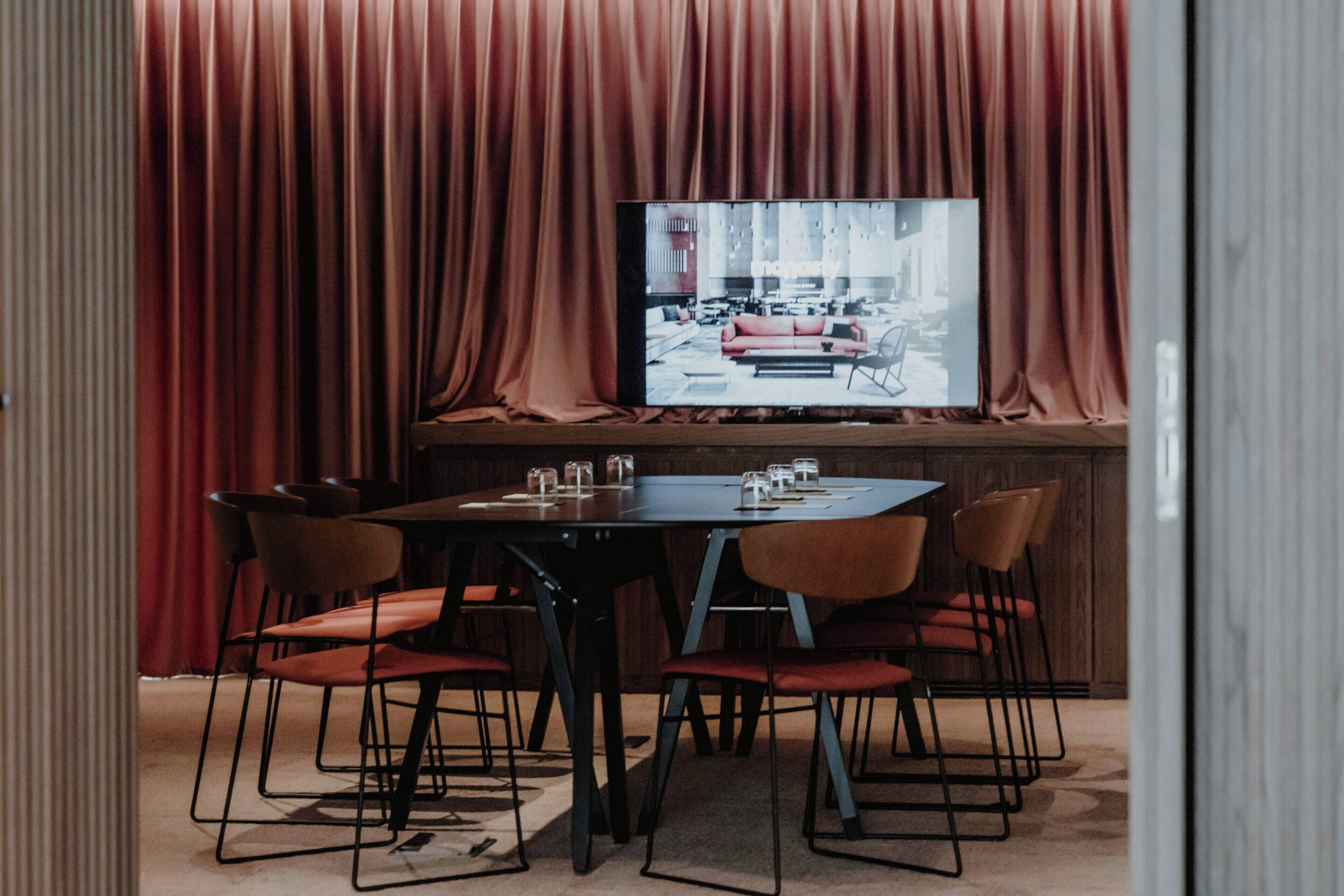 A conference room with a large table, six chairs, and a television screen displaying an image.