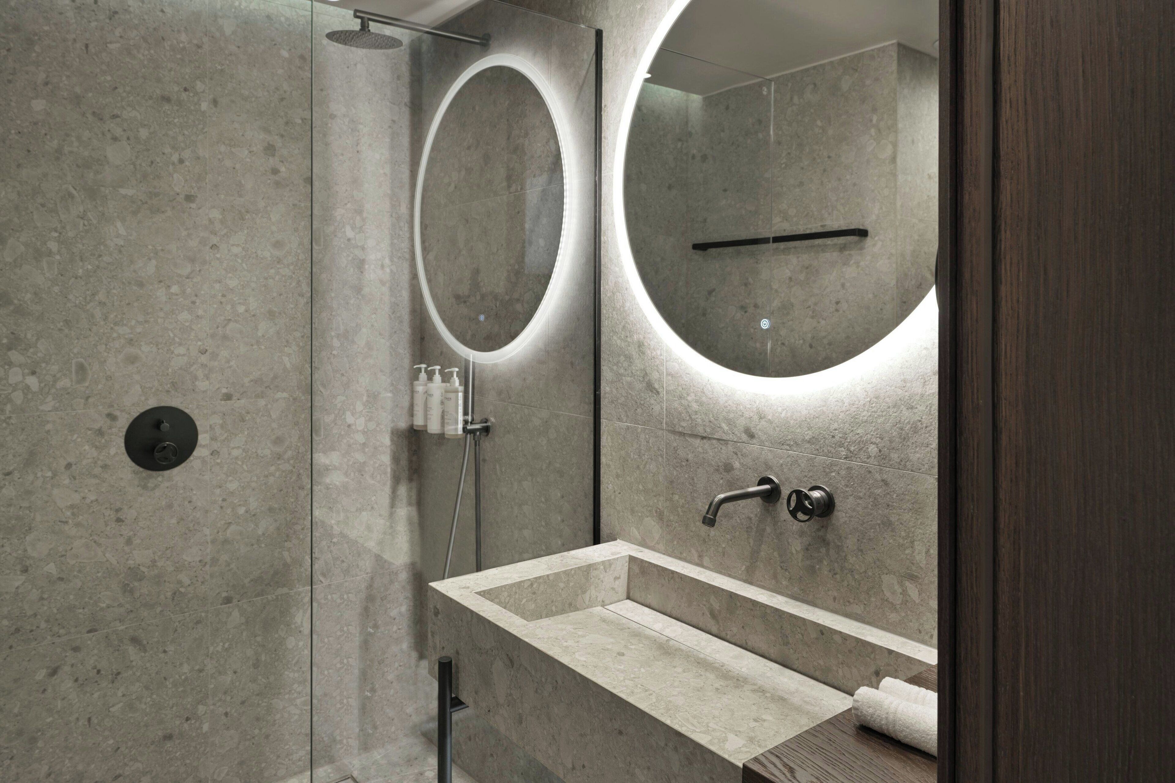 Un baño moderno con un lavamanos rectangular, un espejo redondo y una zona de ducha.
