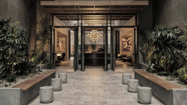 A modern lobby with a central reception desk, a chandelier, and planters with tropical plants. - MonAsty, Thessaloniki, Autograph Collection (Thessaloniki)