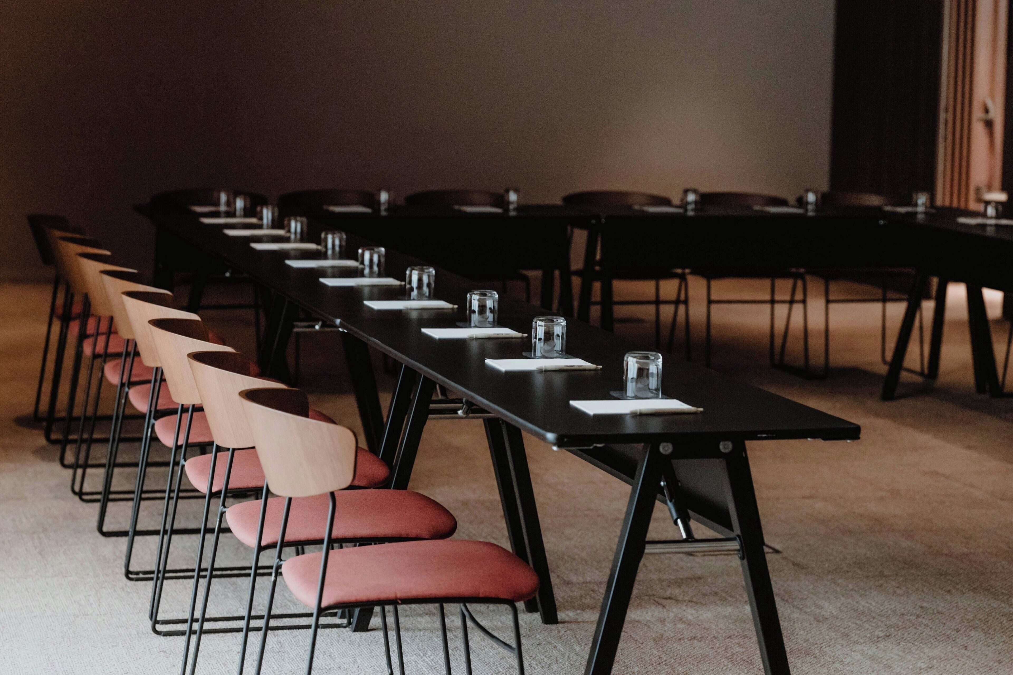 Un salón de conferencias con filas de sillas y mesas, equipado con vasos de agua y blocs de notas.