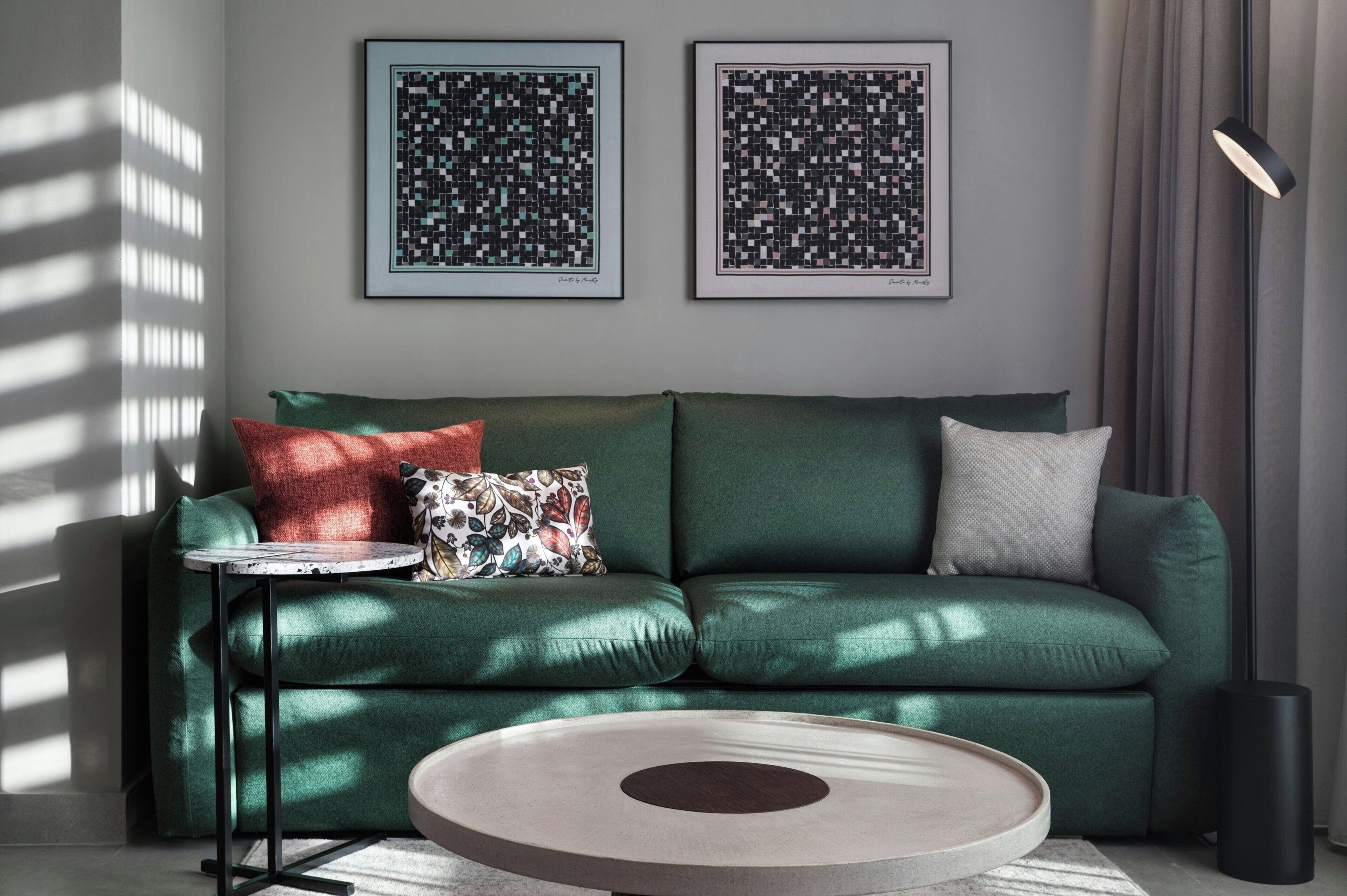A modern living room with a green sofa, a small round table, and two framed abstract artworks on the wall.