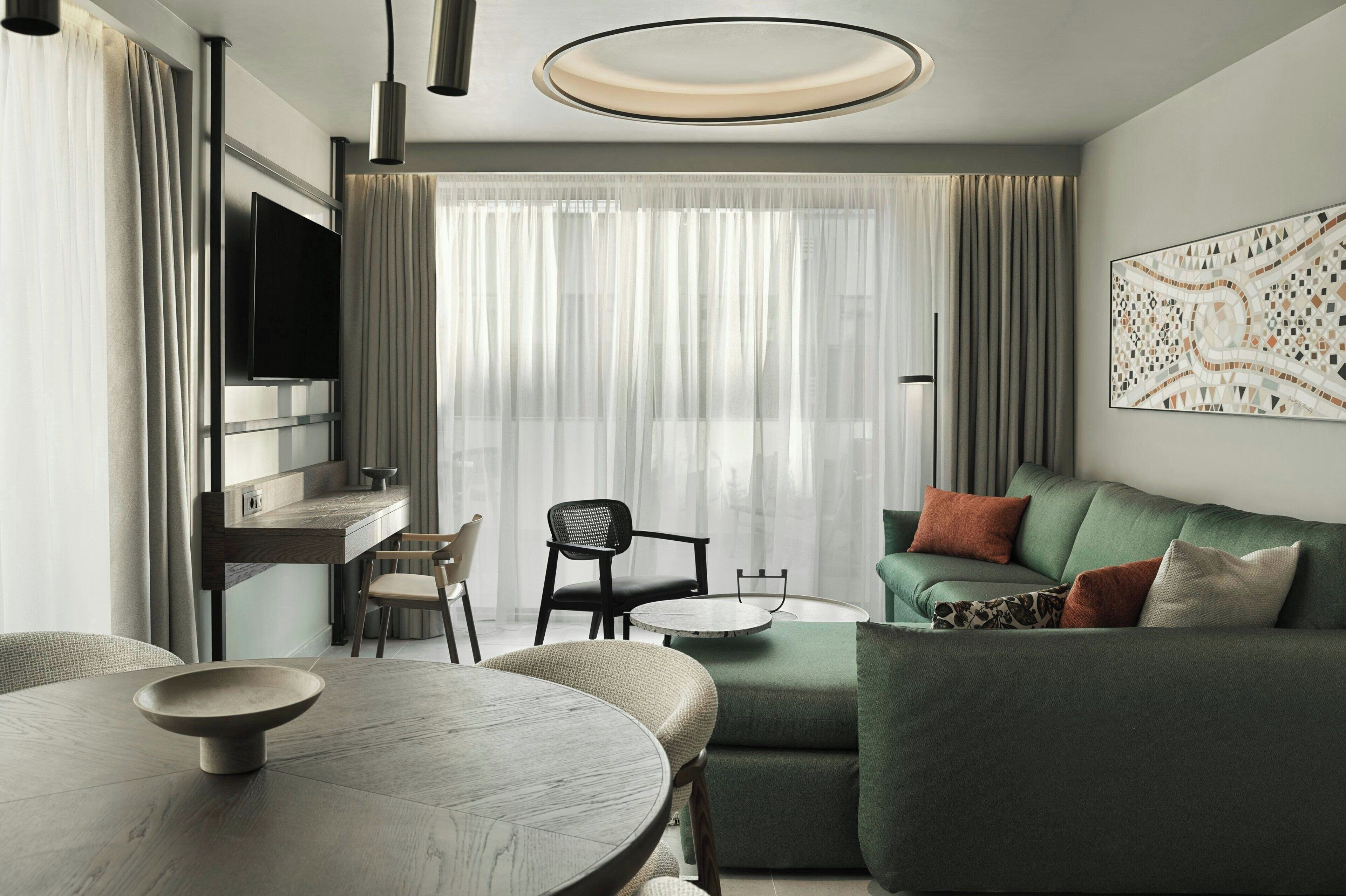 A modern living room with a green sofa, a round dining table, and a flat-screen TV mounted on the wall.
