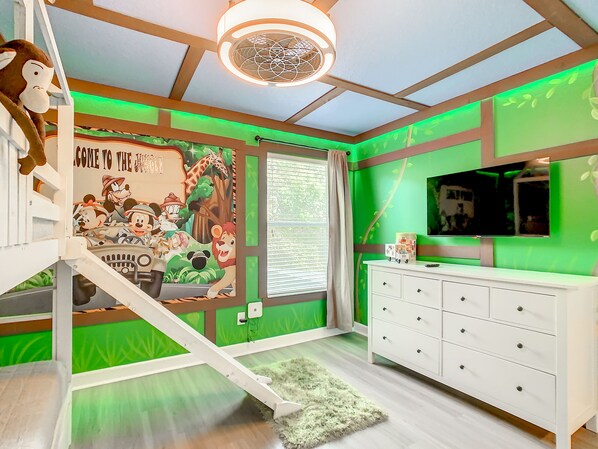 A room with a green-themed wall, a white dresser, a TV, and a poster of animated characters.