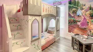 Een kinderkamer met een stapelbed, een muurschildering van een sprookjesdecor en een klein tafeltje met een theepot.