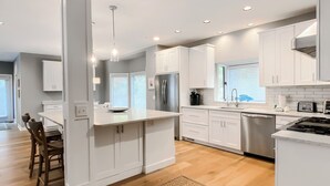 A modern kitchen with white cabinetry, a central island, and a dining area with wooden chairs. - 6 Painted Bunting at The Sea Pines Resort (Hilton Head Island)