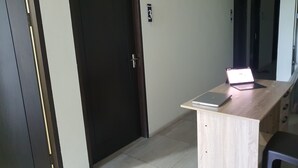 Een gang met een houten bureau, een laptop en een deur met een nummerbord.