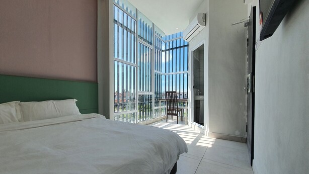 Een moderne hotelkamer met een groot bed, een balkon met een stoel en uitzicht op de stad.