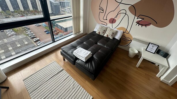 Una camera da letto moderna con un'ampia finestra, un divano letto in pelle nera, vista sulla città e un murale.