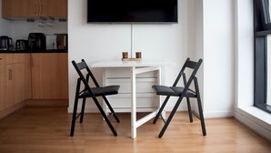 Una cucina moderna con mobili in legno, un tavolo da pranzo bianco, due sedie nere e una TV a schermo piatto montata a parete.
