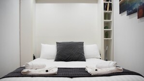 Un letto rifatto con cura, con biancheria da letto bianco e grigio, un cuscino grigio e due asciugamani piegati.