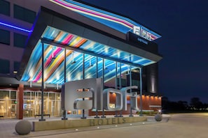 Un hotel con fachada moderna, amplios ventanales de vidrio y un diseño de techo colorido.
