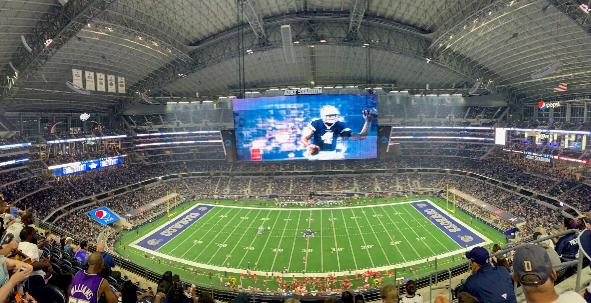 A large indoor stadium with multiple levels of seating, a large screen displaying a sports event, and a Pepsi logo.