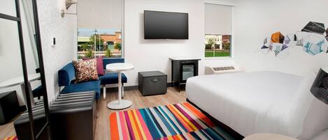 A modern hotel room with a large bed, a flat-screen TV, a small desk, and a colorful striped rug.