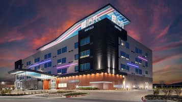 Un edificio hotelero moderno con techo plano, múltiples ventanas y un cartel llamativo.
