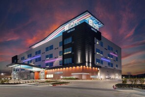 Un edificio hotelero moderno con techo plano, múltiples ventanas y un cartel llamativo.