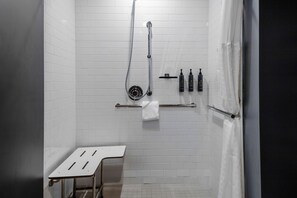 A modern bathroom with white tiled walls, a shower with a handheld showerhead, a towel rack, and a small table.