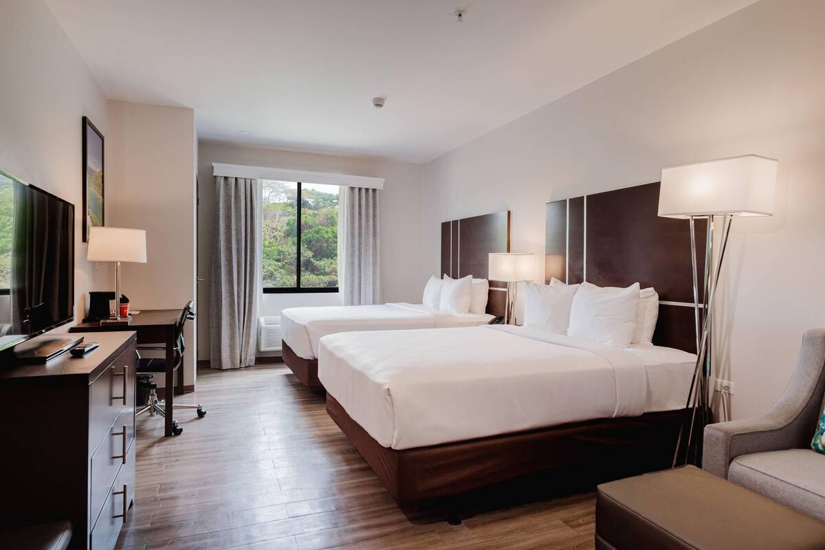 A hotel room with two beds, a desk, a chair, and a TV.