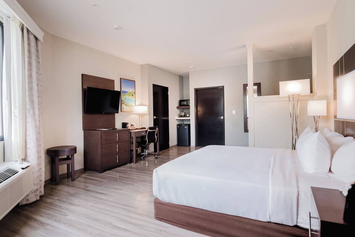 A hotel room with a bed, desk, chair, TV, and a view of the outdoors.