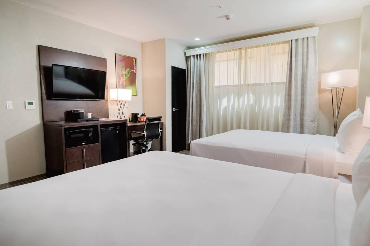 A hotel room with two beds, a TV, a desk with a computer, a microwave, and a coffee maker.