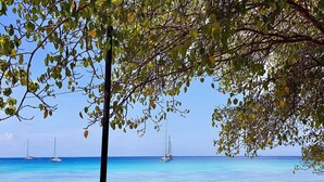 A beach with clear turquoise water, sailboats, and rocky outcrops.