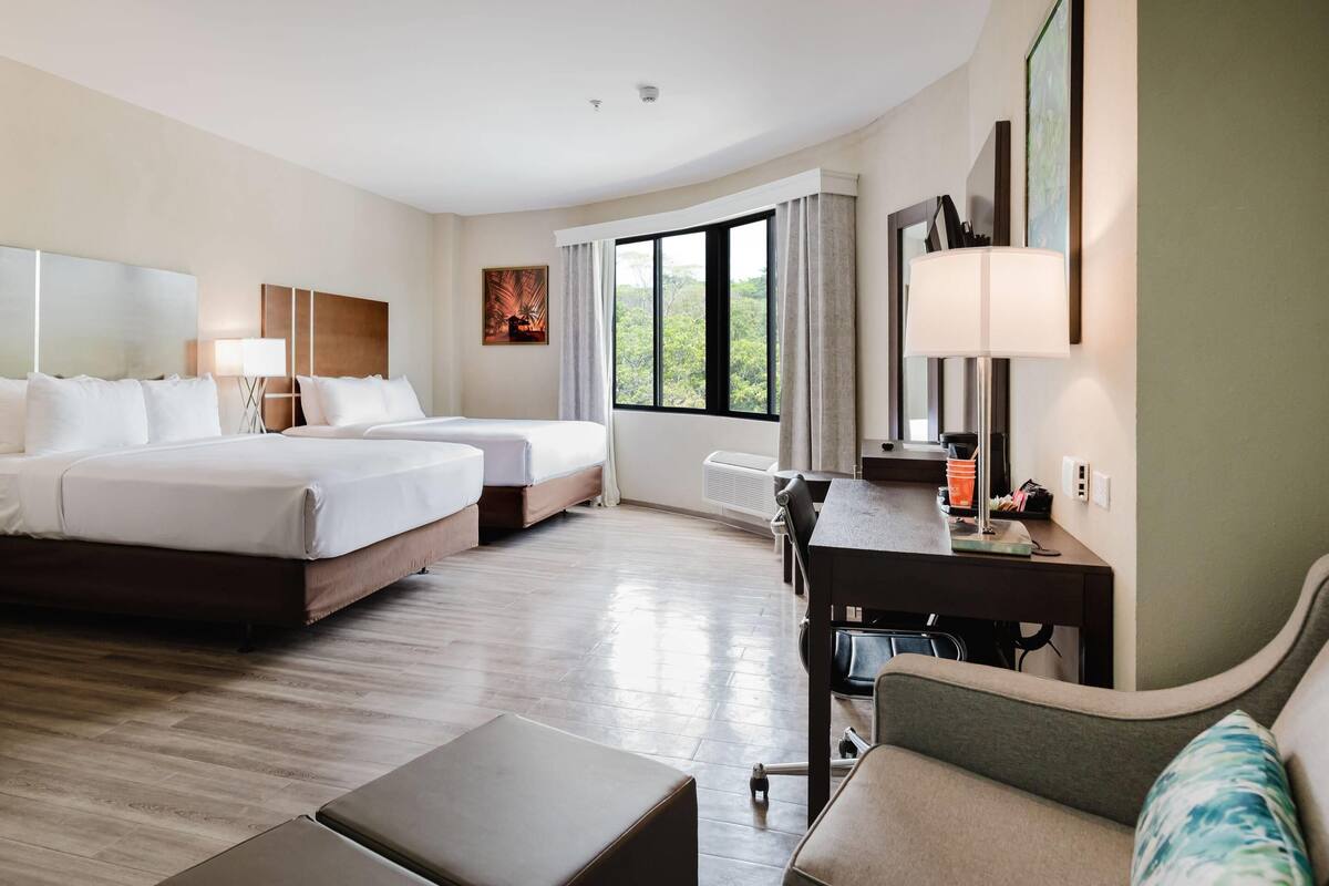 A hotel room with two beds, a desk, and a sofa.