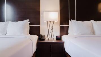 Una camera d'albergo con due letti, un comodino con lampada, un telefono e una sveglia digitale.