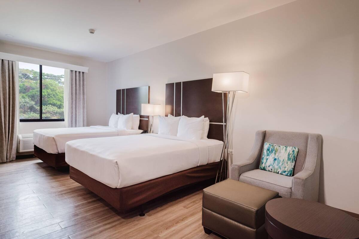A hotel room with two beds, a sofa, a chair, and a lamp.
