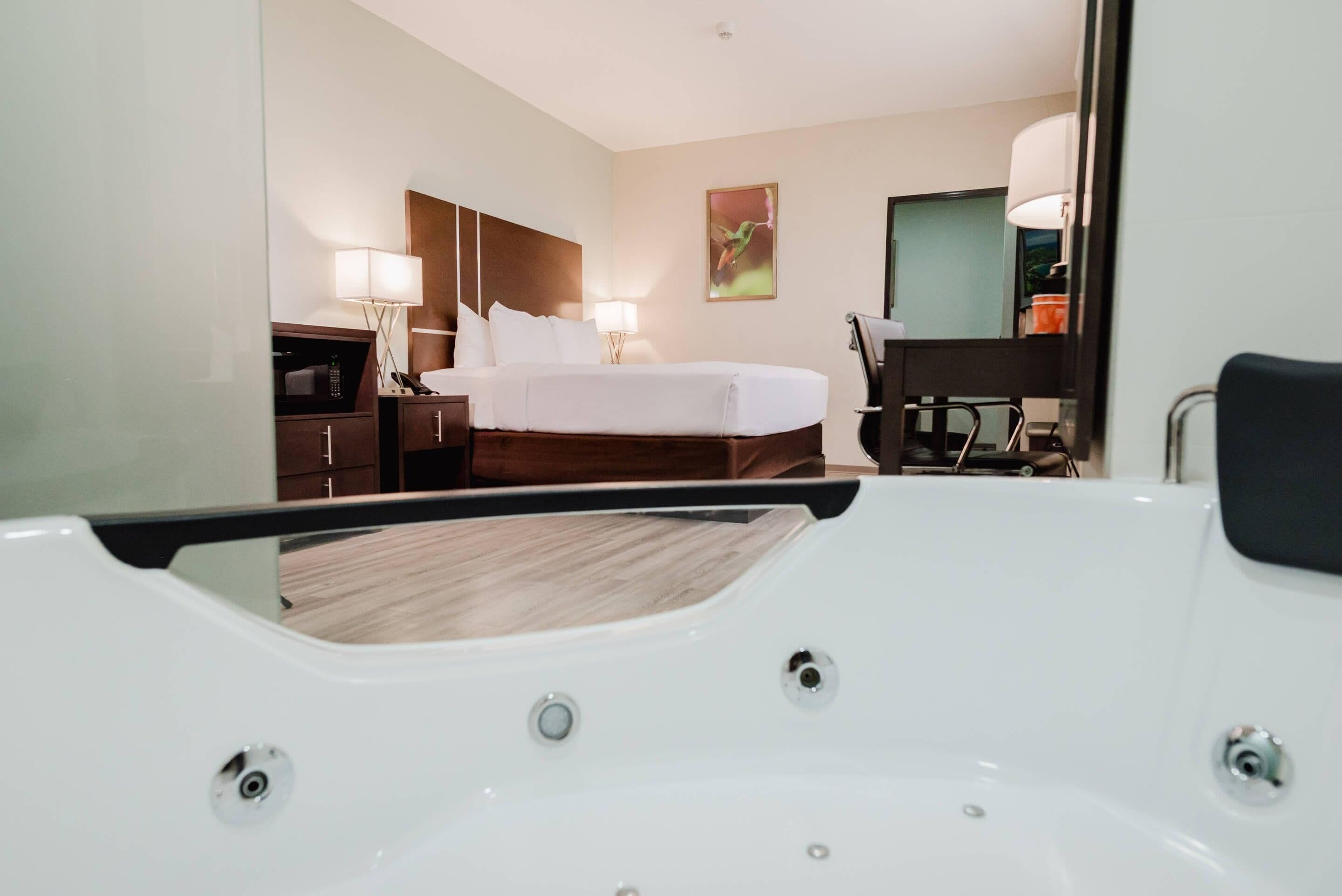 A hotel room with a bed, bedside tables, a desk, a chair, and a large mirror.