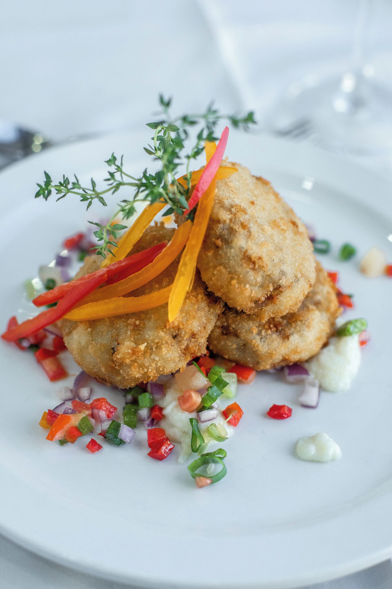 A plate of food with breaded items, garnished with herbs and colorful vegetables.