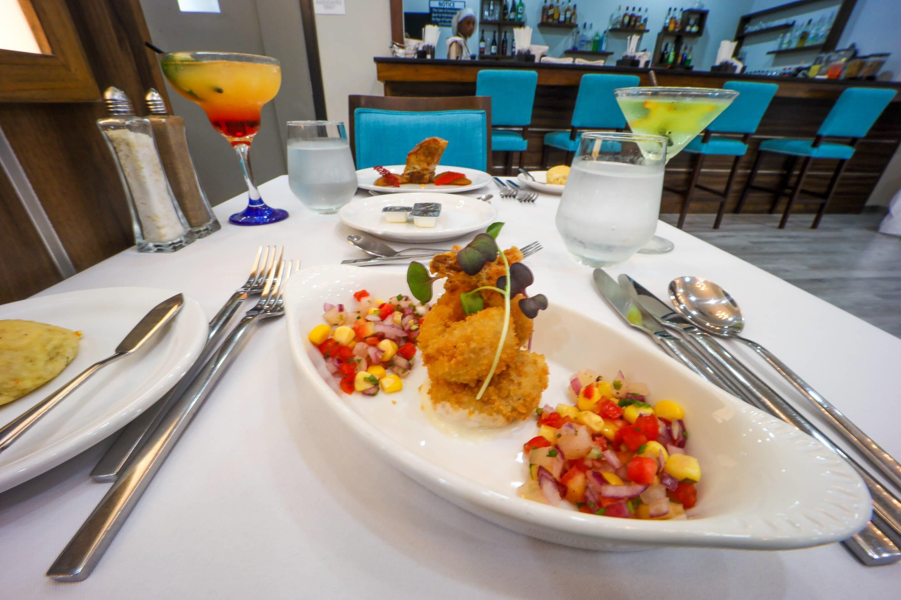 Une table à manger dressée avec une variété de plats, notamment un filet de poisson, une salsa colorée et un cocktail.