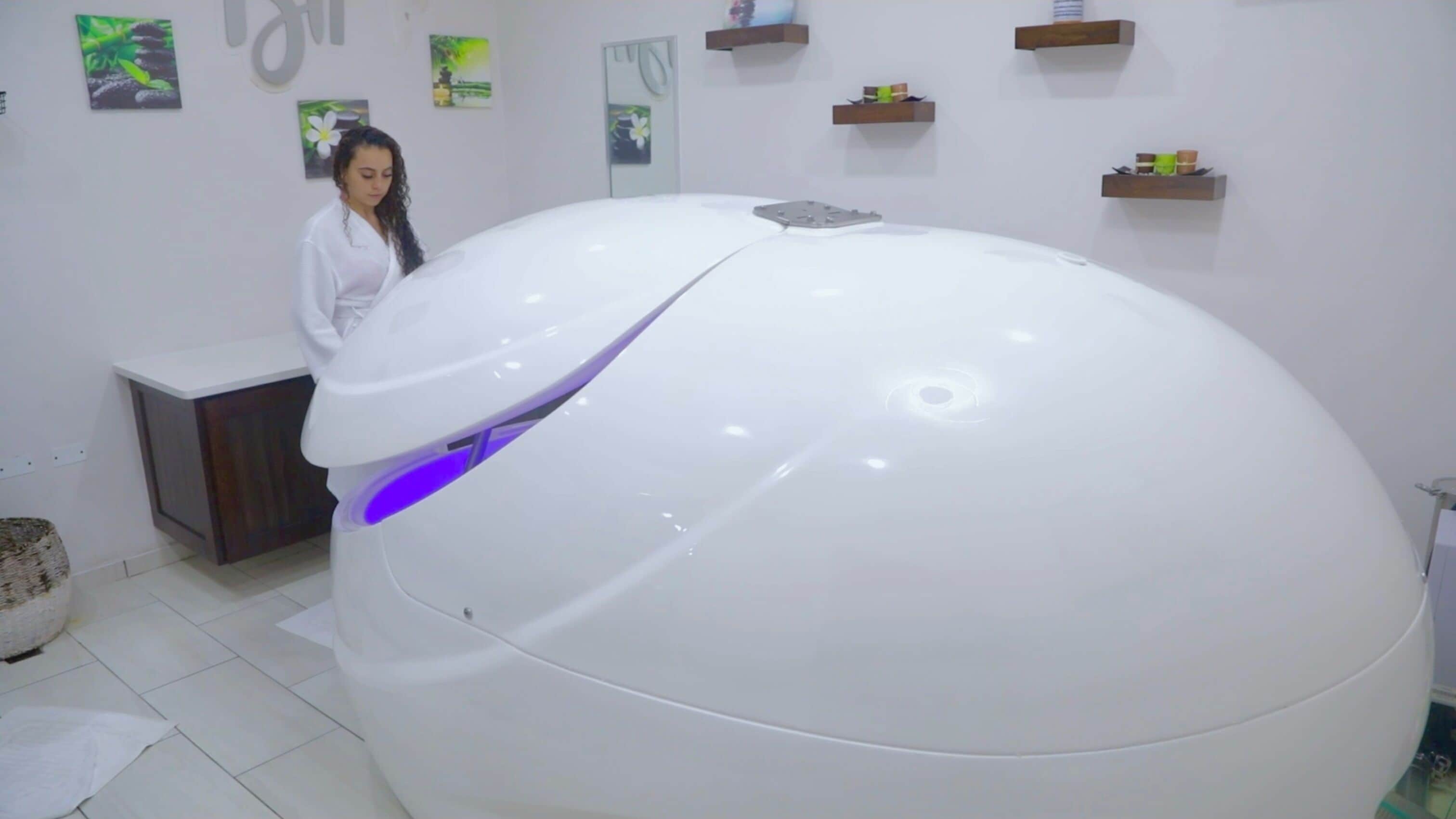 A large, white, spherical object with a purple light on one side, possibly a piece of art or equipment, in a room with white walls and shelves with items on them.