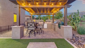 Patio esterno con pergola, arredi e zona barbecue.