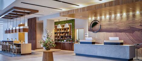 A modern reception area with a wooden reception desk, a seating area with chairs, a large potted plant, and a wall with a textured design.