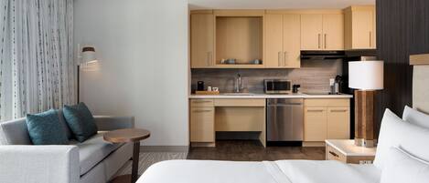 Une chambre d’hôtel moderne équipée d’un canapé, d’un lit, d’une petite table, d’un coin cuisine avec un four à micro-ondes et d’une lampe.