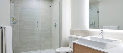 Un baño moderno con ducha de vidrio, lavamanos blanco y tocador de madera.