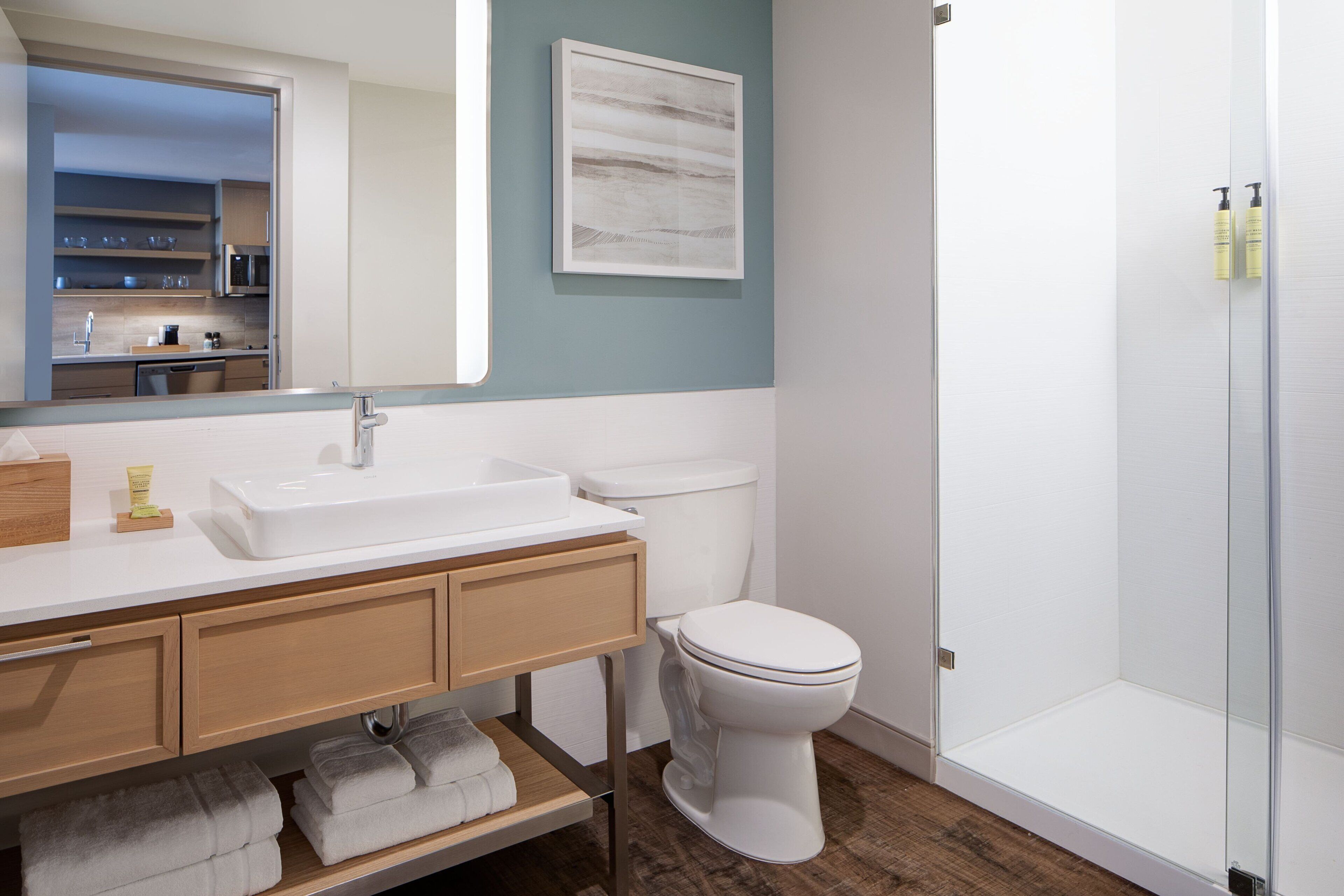Une salle de bain moderne avec un lavabo blanc, un meuble-lavabo en bois et une cabine de douche en verre.