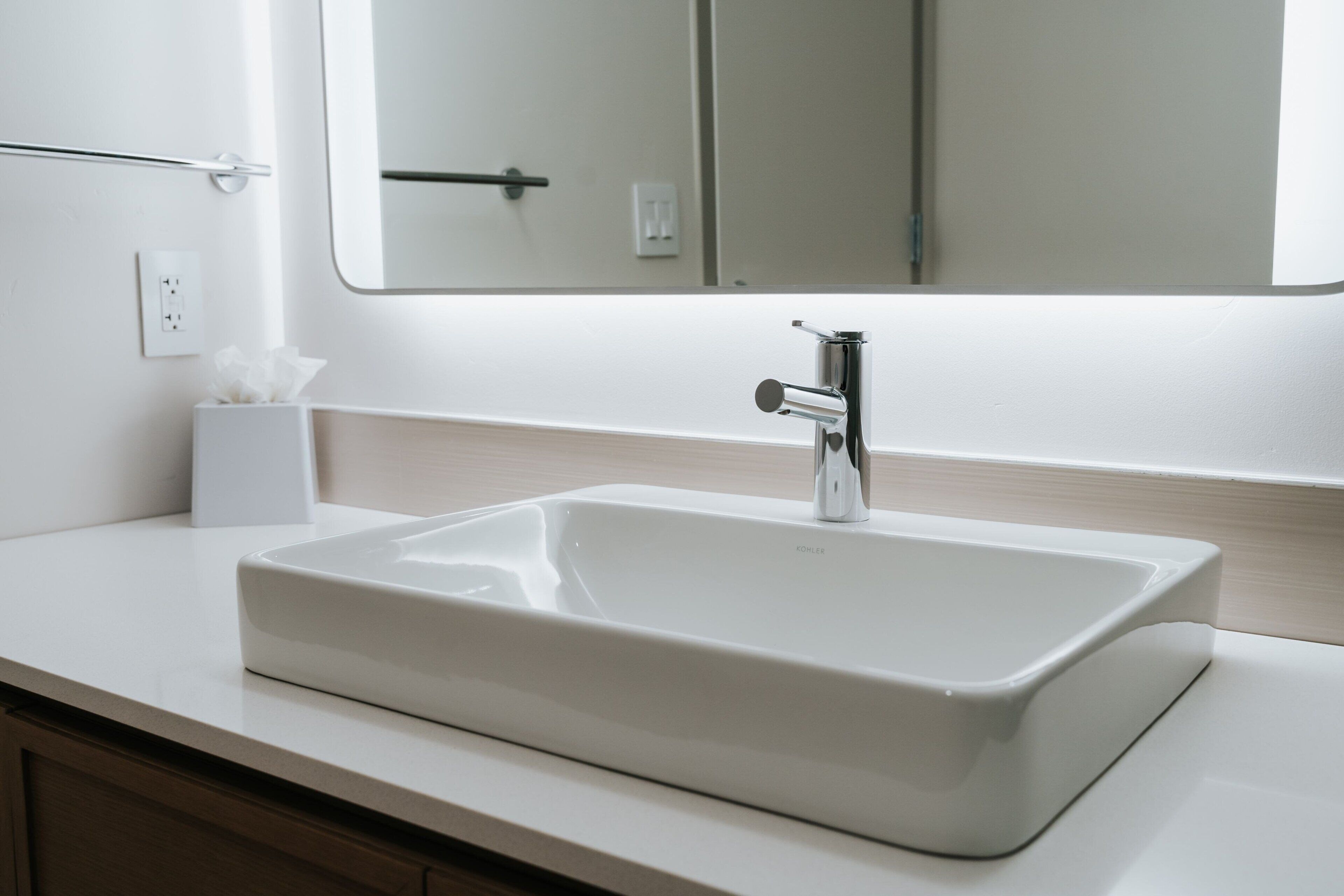 A modern bathroom with a white sink, chrome faucet, and a large mirror above it.