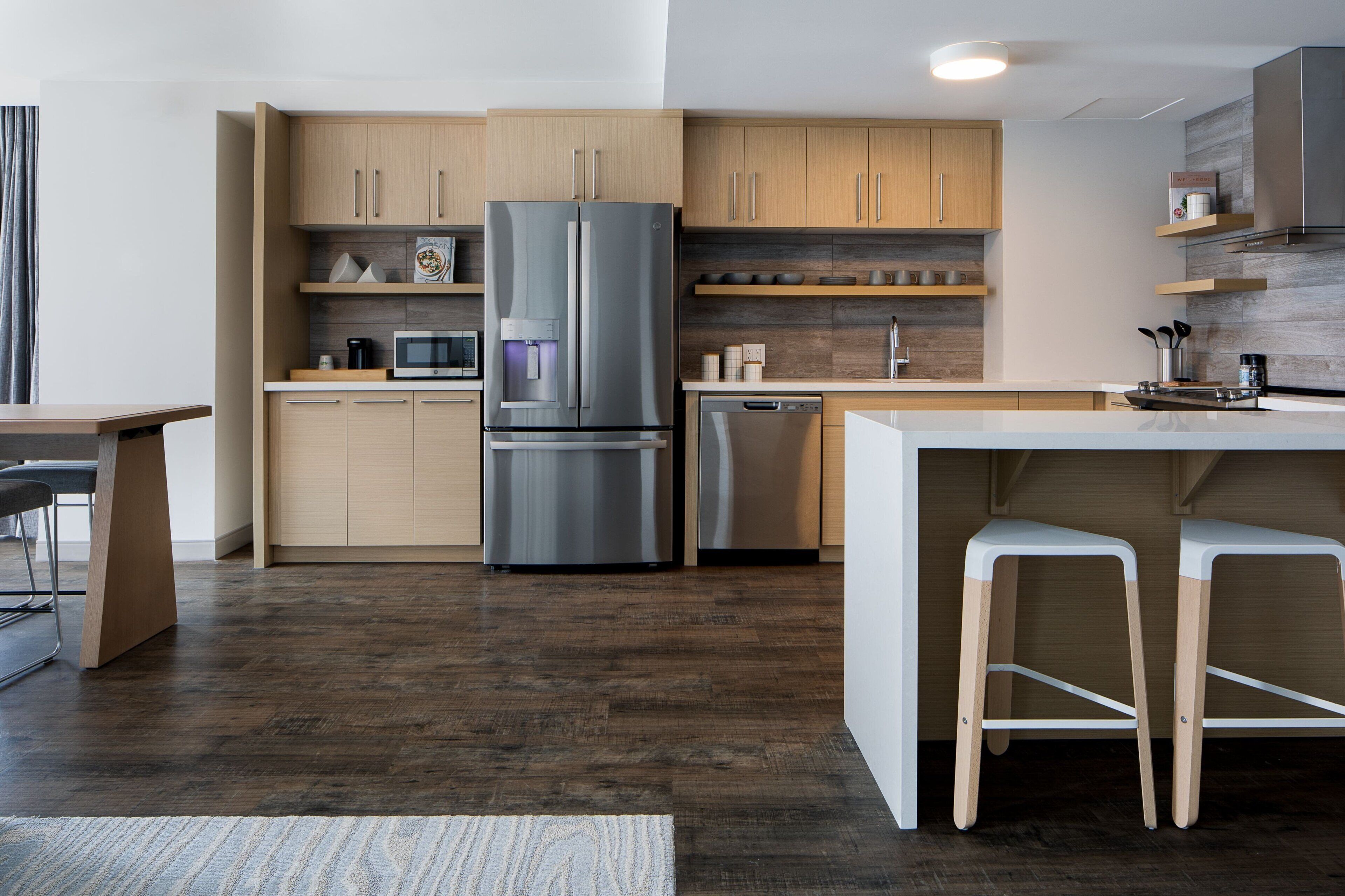 Une cuisine moderne avec des meubles en bois, un réfrigérateur en acier inoxydable, un lave-vaisselle et un coin bar équipé de tabourets.