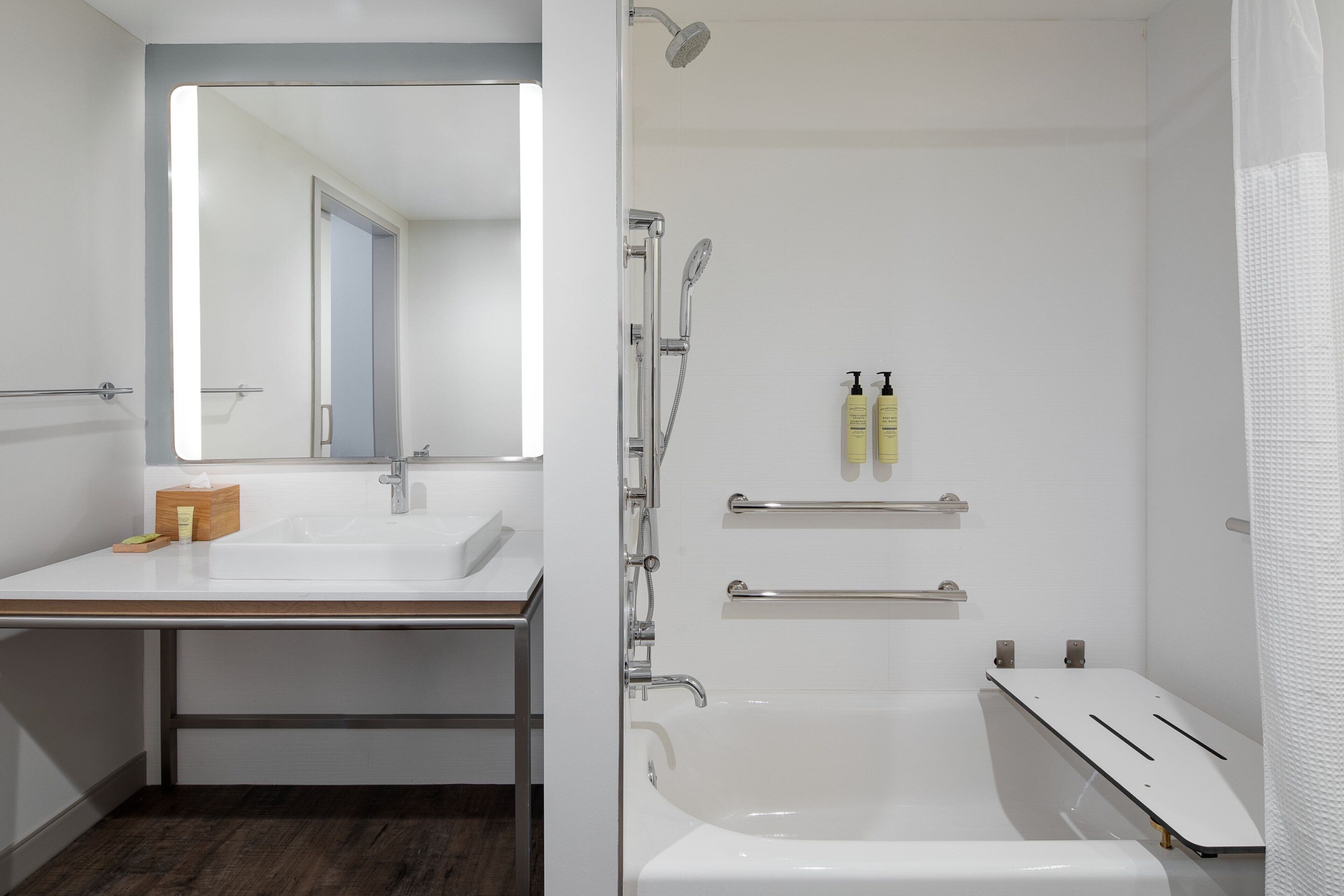 Ein modernes Badezimmer mit Waschbecken, Spiegel, Dusche und zwei Ablagen mit Pflegeprodukten.
