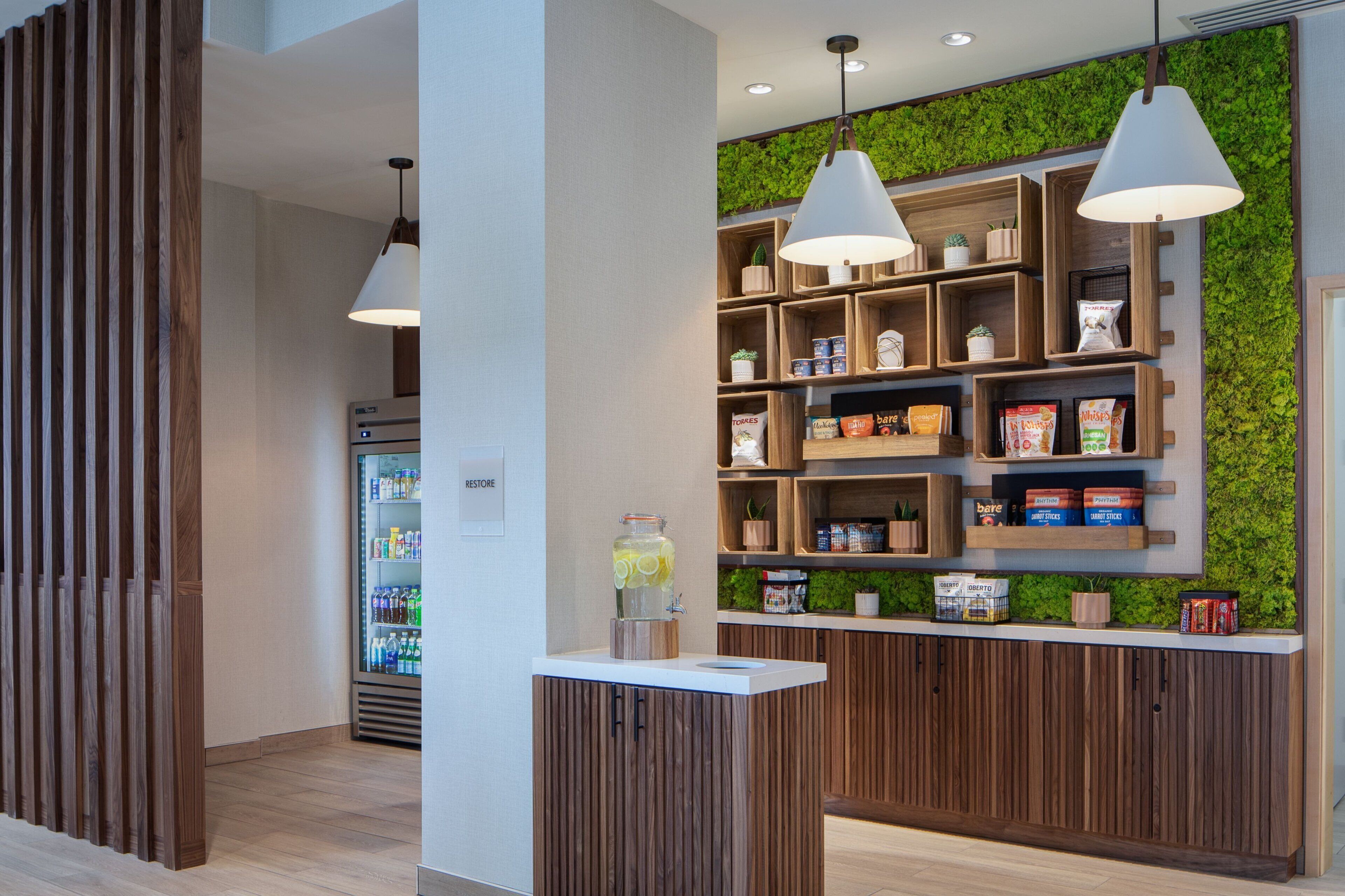 A modern reception area with wooden paneling, a refrigerated beverage dispenser, and a wall-mounted shelf with snacks and a planter.