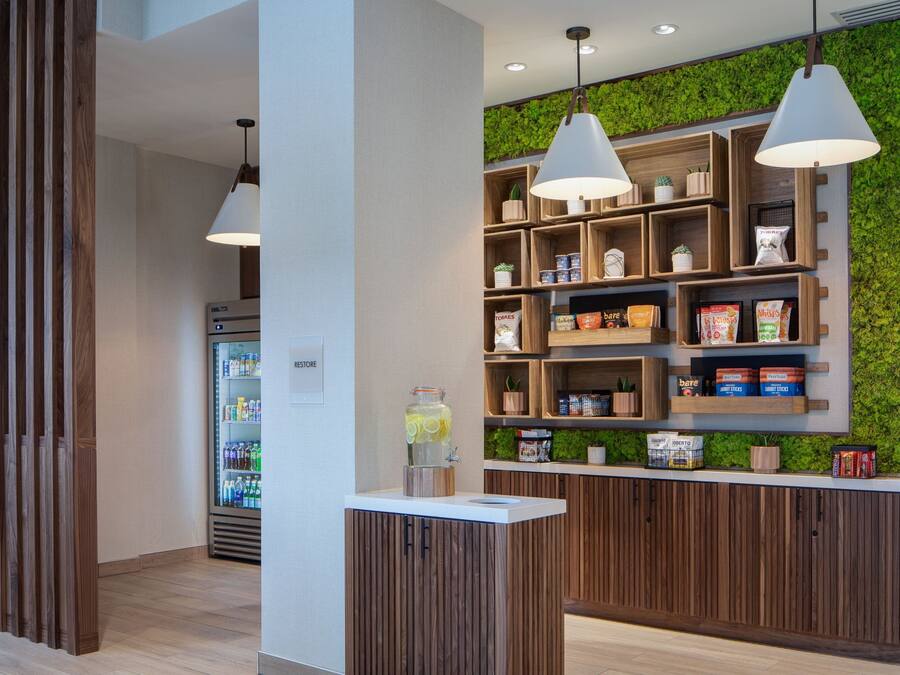 A modern reception area with wooden paneling, a refrigerated beverage dispenser, and a wall-mounted shelf with snacks and a planter.