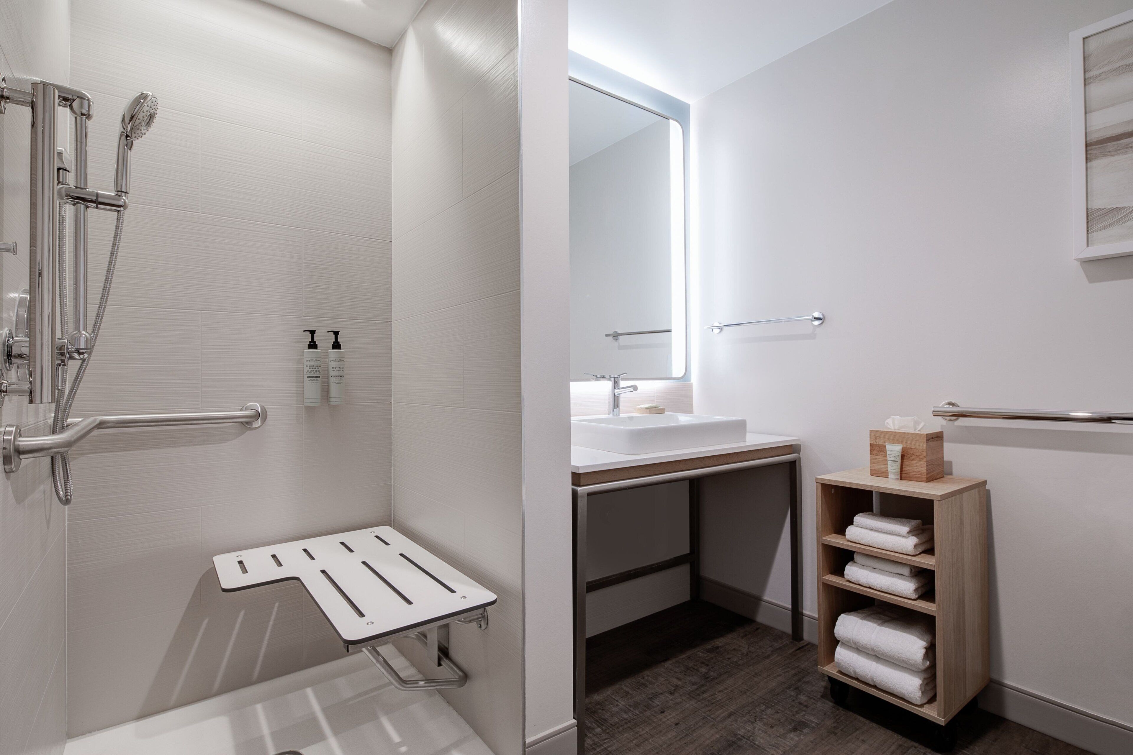 A modern bathroom with a walk-in shower, a bathtub, a sink, and a wooden shelf with towels.
